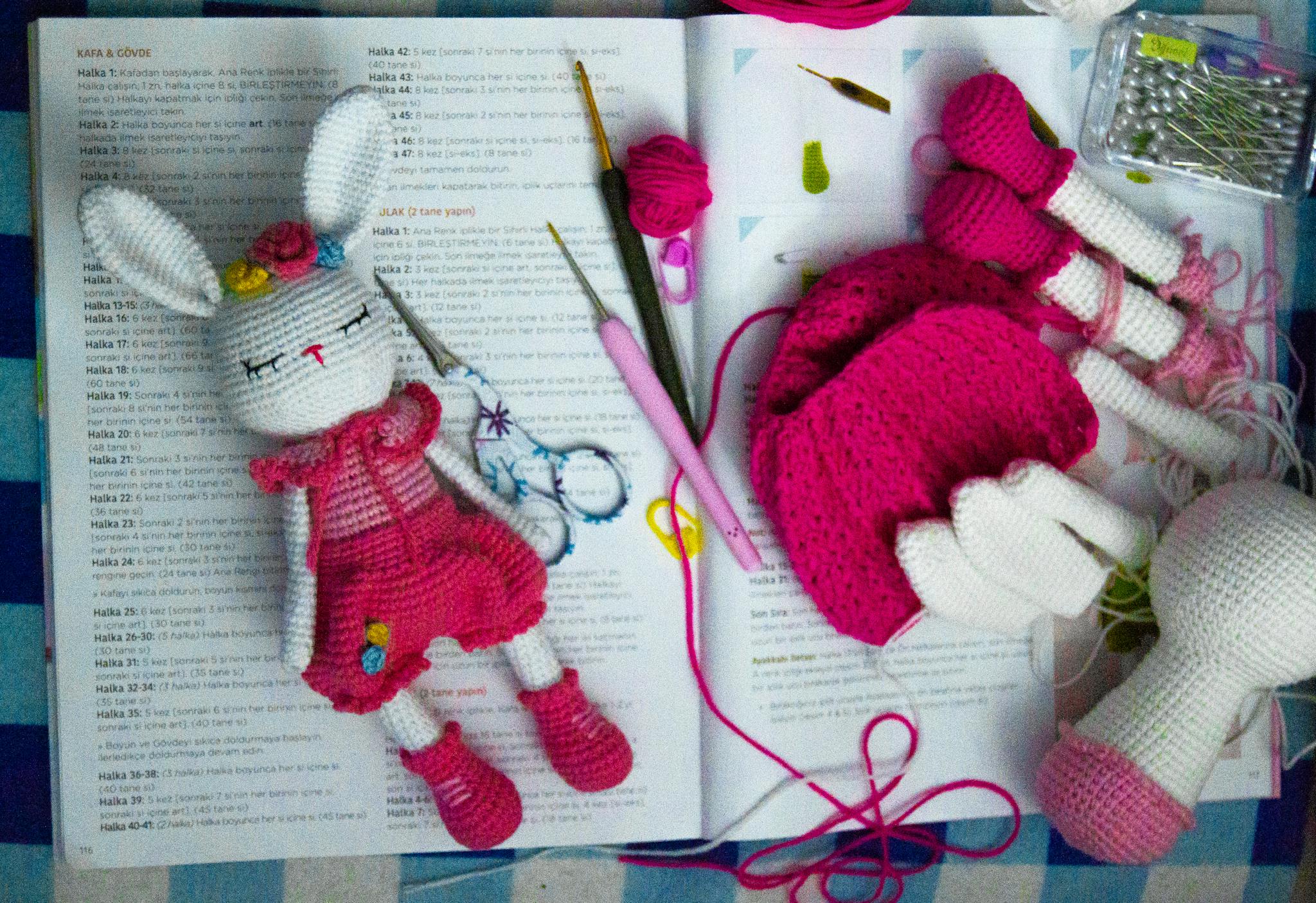 A handmade crochet bunny toy with crochet tools on a crochet handbook.